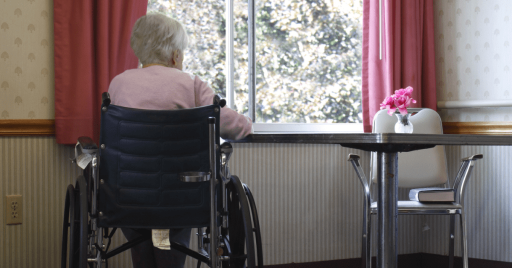 Elderly woman in a wheelchair looking out a window in a nursing home