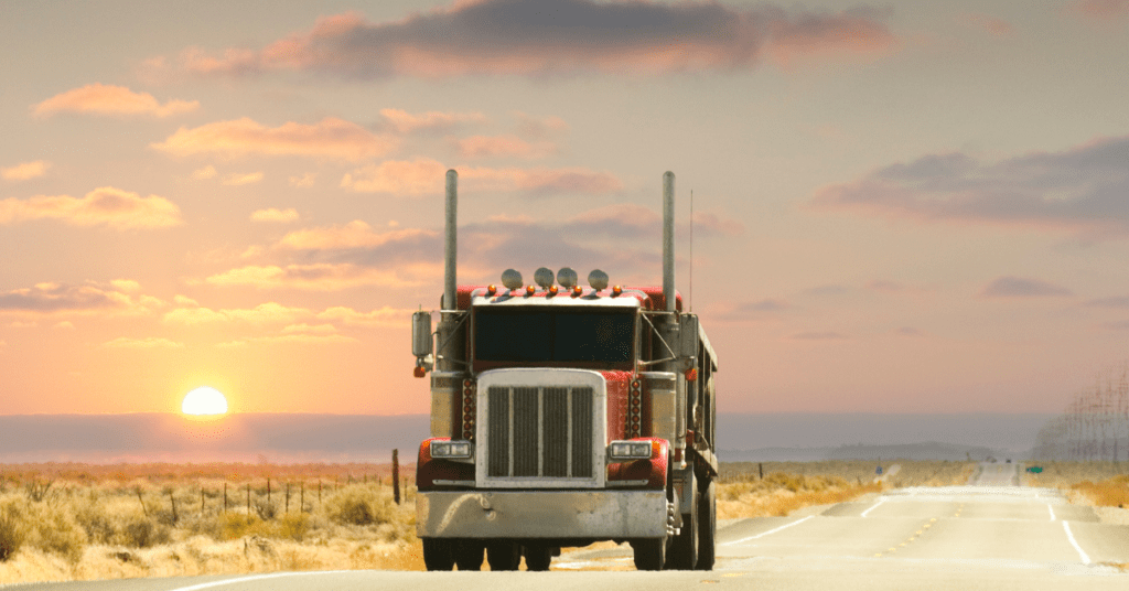 Large semi-truck driving on a highway at sunset