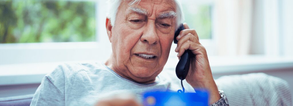 Elderly man on the phone, reviewing a credit card, symbolizing the risk of elder fraud and financial scams