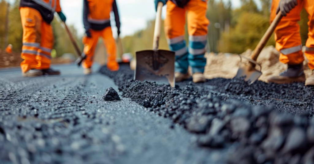 Road construction workers in orange safety gear paving asphalt in a highway work zone, emphasizing the importance of driver awareness and worker safety.