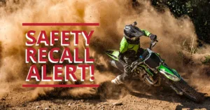 An off-road dirt bike rider skids through dirt with dust cloud, paired with bold red text reading “Safety Recall Alert”