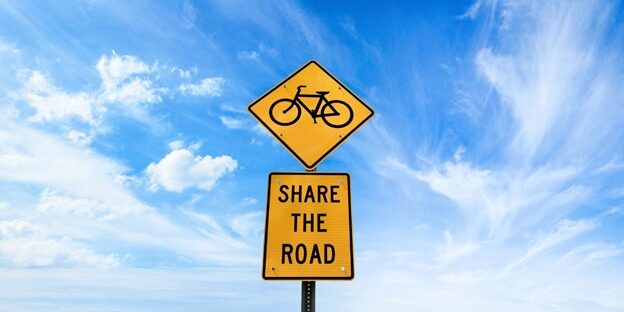 Yellow road sign reading 'Share the Road' with a bicycle symbol, promoting cyclist safety under a clear blue sky